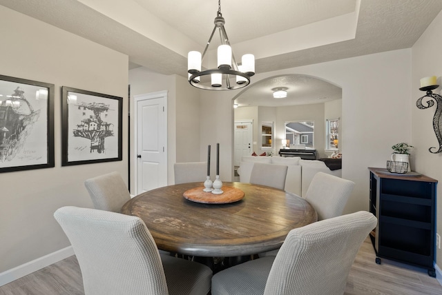 dining area with a raised ceiling, light hardwood / wood-style flooring, and an inviting chandelier