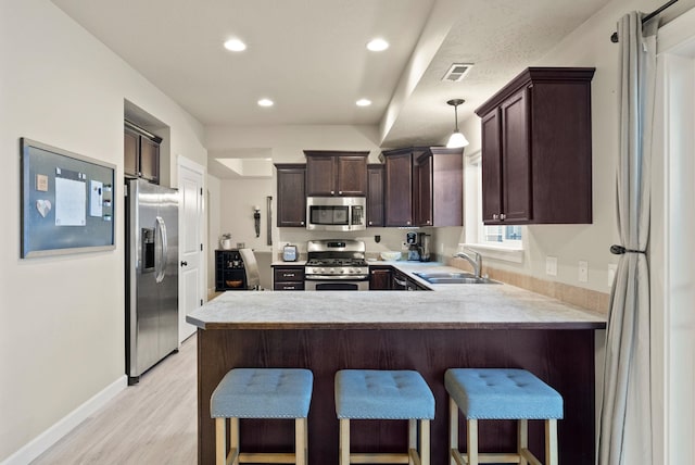 kitchen featuring sink, stainless steel appliances, light hardwood / wood-style flooring, pendant lighting, and a kitchen bar