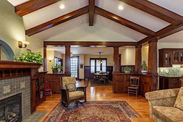 living room with a fireplace, lofted ceiling with beams, light hardwood / wood-style flooring, and ornate columns