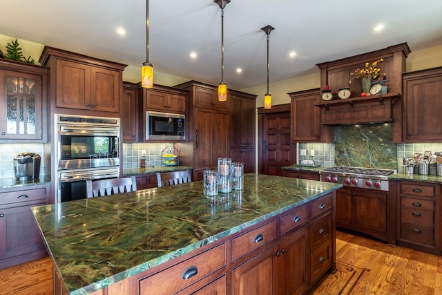 kitchen featuring stainless steel appliances, light hardwood / wood-style flooring, dark stone countertops, a kitchen island, and hanging light fixtures