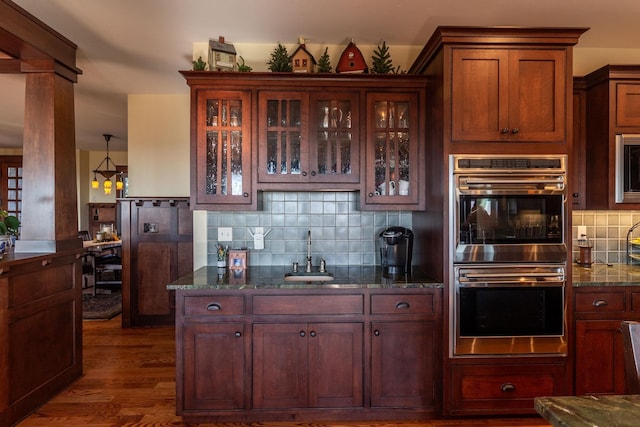 kitchen with decorative backsplash, appliances with stainless steel finishes, dark hardwood / wood-style flooring, dark stone counters, and sink