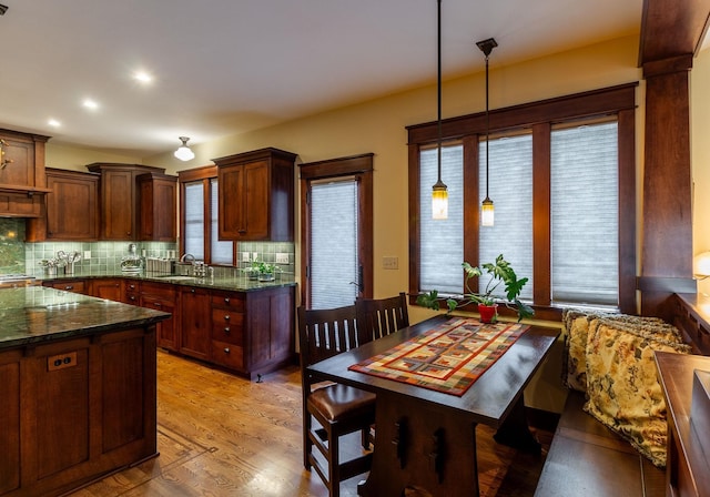 kitchen featuring sink, light hardwood / wood-style flooring, backsplash, dark stone counters, and pendant lighting