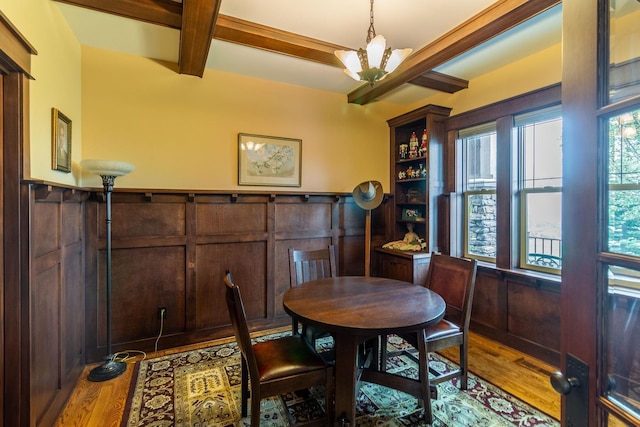 dining space featuring wood-type flooring, wood walls, a notable chandelier, and beam ceiling