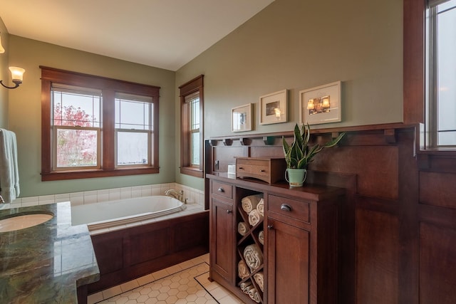 bathroom featuring tile patterned flooring, vanity, tiled bath, and vaulted ceiling