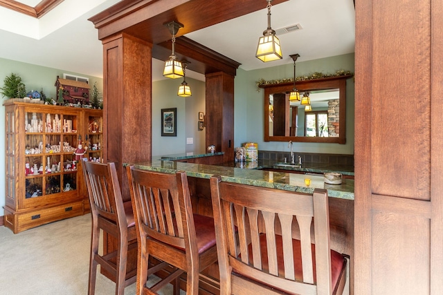 bar featuring ornate columns, hanging light fixtures, light colored carpet, and sink