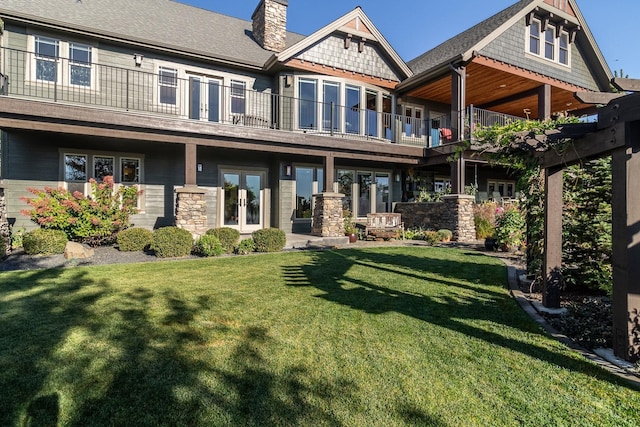 rear view of house with a balcony, a yard, and french doors