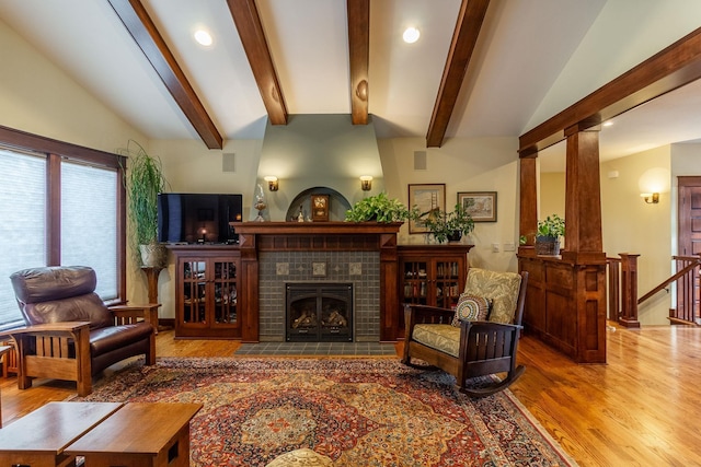 living room with lofted ceiling with beams, hardwood / wood-style flooring, decorative columns, and a tiled fireplace