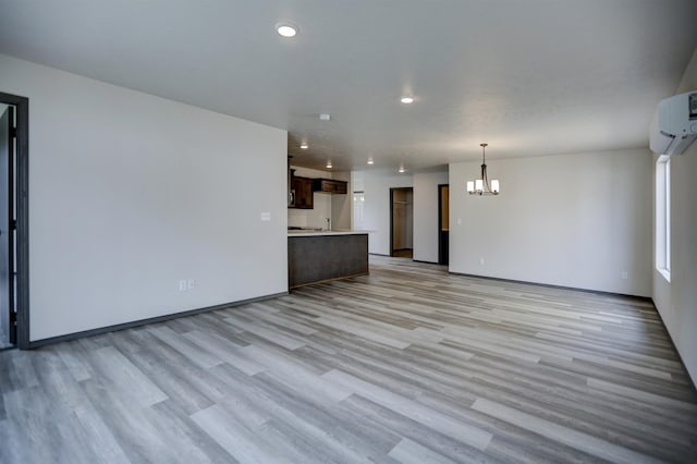 unfurnished living room with light wood finished floors, recessed lighting, a chandelier, and an AC wall unit