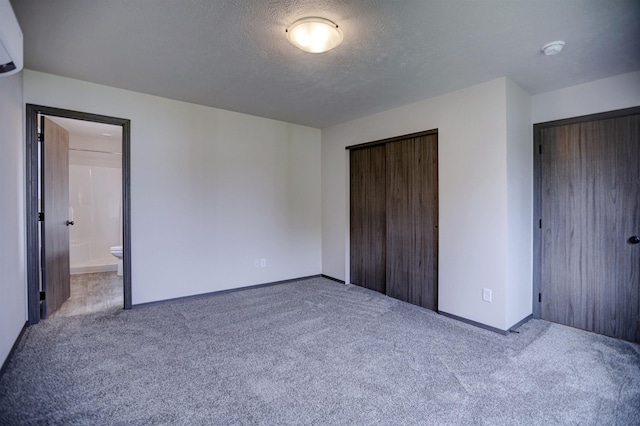 unfurnished bedroom with a textured ceiling, a wall mounted AC, carpet floors, and baseboards