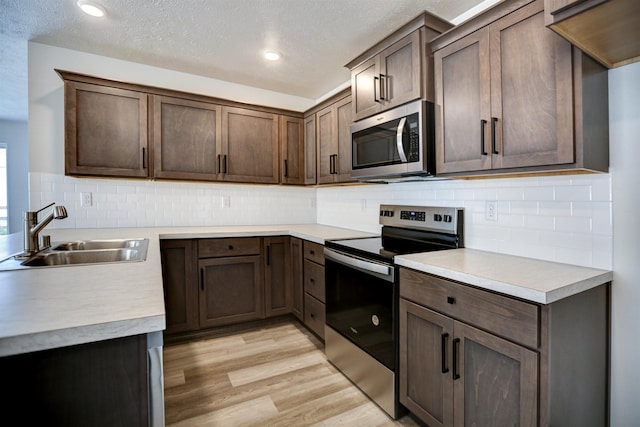 kitchen with light countertops, stainless steel appliances, light wood-type flooring, and a sink