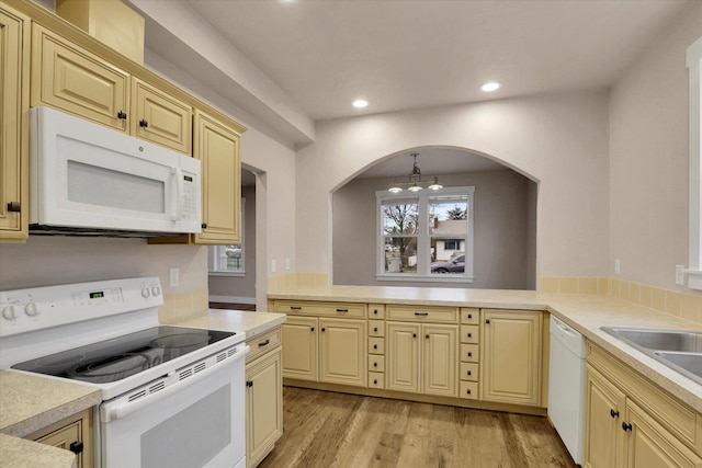 kitchen with kitchen peninsula, light wood-type flooring, white appliances, an inviting chandelier, and hanging light fixtures