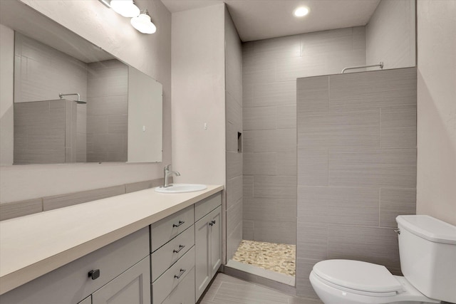 bathroom with tile patterned floors, vanity, tiled shower, tile walls, and toilet