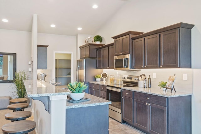 kitchen featuring light stone countertops, appliances with stainless steel finishes, kitchen peninsula, and a kitchen breakfast bar