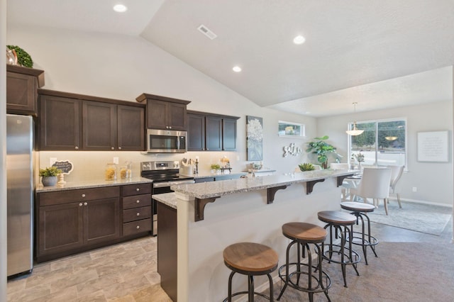 kitchen featuring a kitchen breakfast bar, light stone counters, an island with sink, decorative light fixtures, and appliances with stainless steel finishes