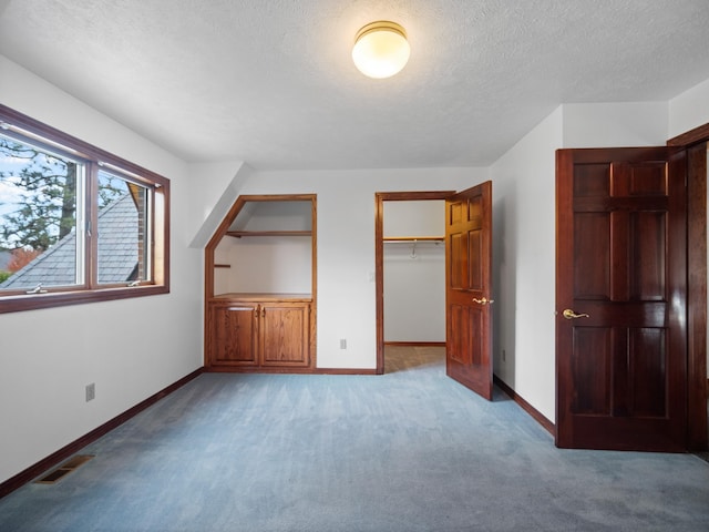 unfurnished bedroom featuring a spacious closet, a closet, light colored carpet, and a textured ceiling