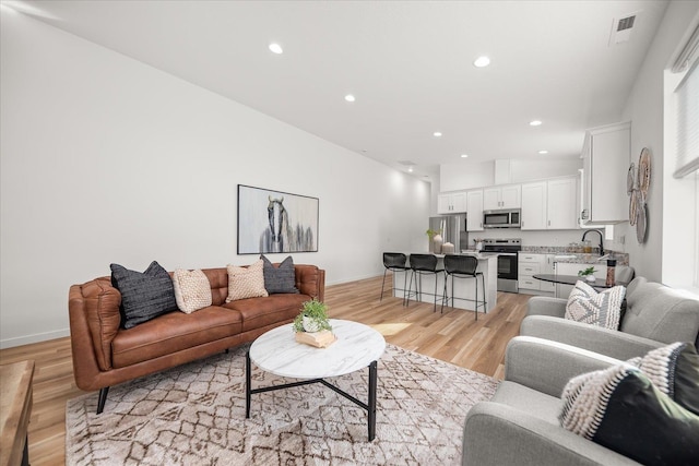 living room with sink, light hardwood / wood-style floors, and lofted ceiling