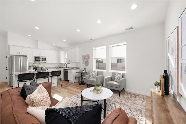 living room with light hardwood / wood-style flooring, lofted ceiling, and sink