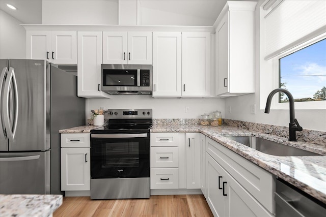 kitchen featuring sink, light wood-type flooring, appliances with stainless steel finishes, light stone counters, and white cabinetry