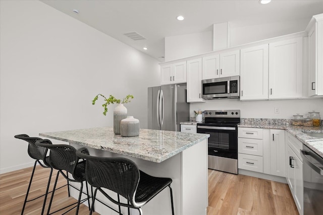 kitchen featuring light wood-type flooring, a kitchen island, a kitchen bar, white cabinetry, and stainless steel appliances