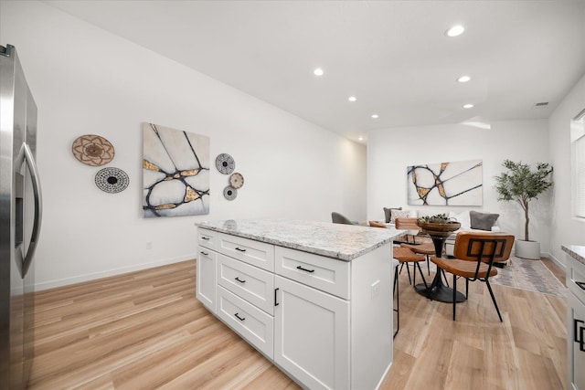 kitchen featuring light stone countertops, stainless steel refrigerator with ice dispenser, light wood-type flooring, a kitchen island, and white cabinetry