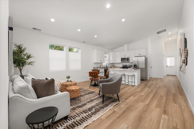 living room with sink, vaulted ceiling, and light wood-type flooring