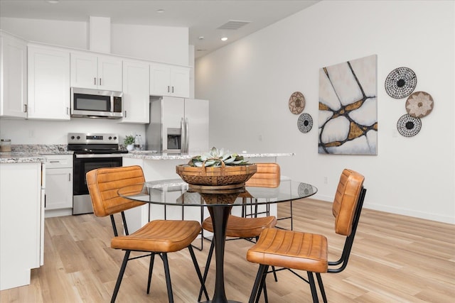 kitchen featuring light stone counters, appliances with stainless steel finishes, a kitchen bar, white cabinets, and light wood-type flooring