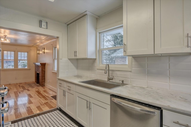 kitchen featuring sink, a brick fireplace, stainless steel dishwasher, tasteful backsplash, and white cabinetry