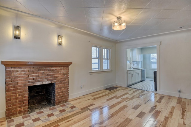 unfurnished living room featuring light wood-type flooring, a brick fireplace, and sink