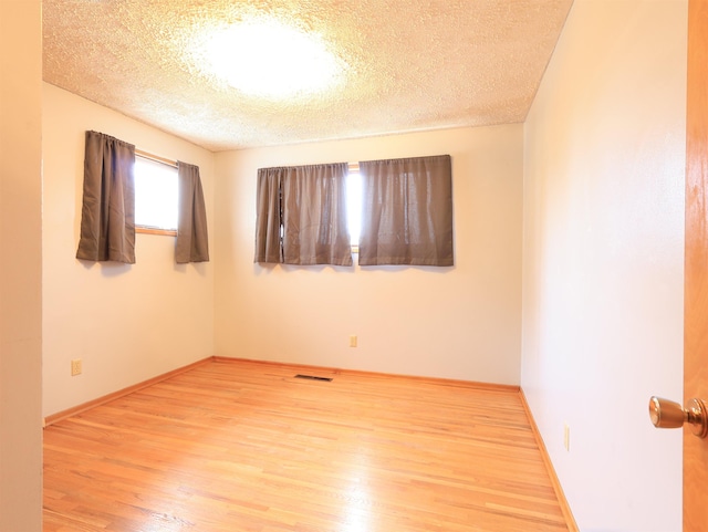 unfurnished room with a textured ceiling and light wood-type flooring