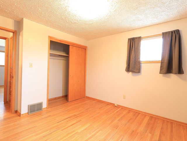 unfurnished bedroom with a textured ceiling, a closet, and light wood-type flooring