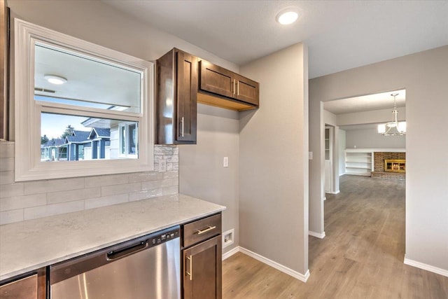 kitchen featuring stainless steel dishwasher, hanging light fixtures, tasteful backsplash, a brick fireplace, and light wood-type flooring