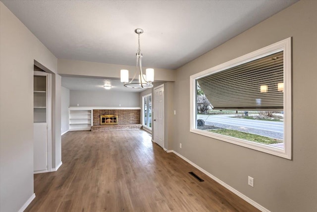 unfurnished dining area featuring wood-type flooring, a fireplace, and a chandelier