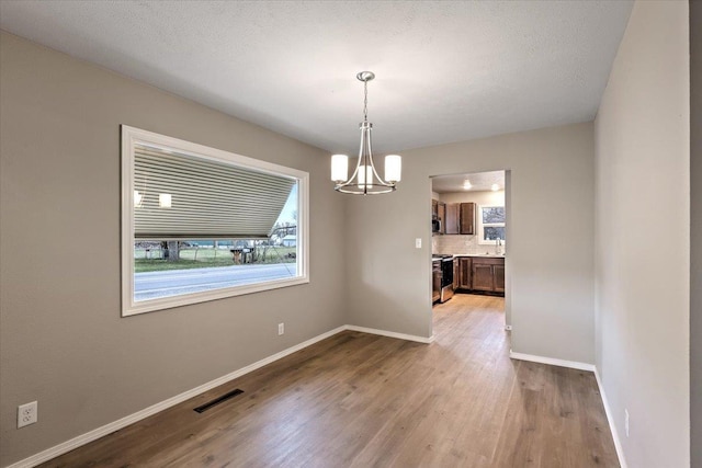 unfurnished dining area featuring light hardwood / wood-style floors, an inviting chandelier, and a textured ceiling