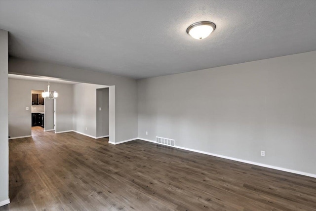 spare room with a notable chandelier, dark hardwood / wood-style flooring, and a textured ceiling