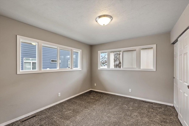 spare room with a textured ceiling and dark colored carpet