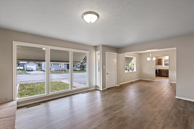 unfurnished living room featuring an inviting chandelier, a textured ceiling, and dark hardwood / wood-style floors