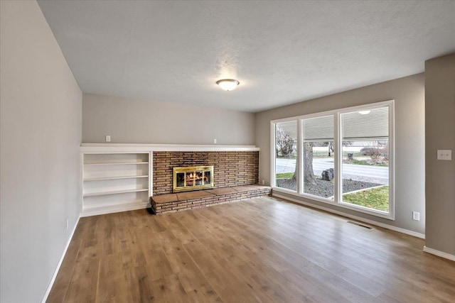 unfurnished living room with built in shelves, a textured ceiling, wood-type flooring, and a fireplace