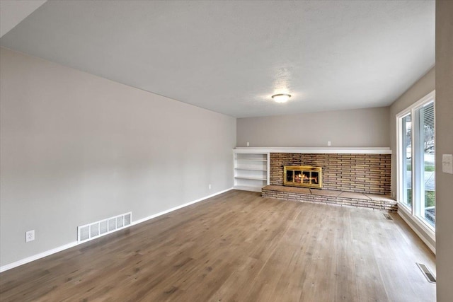 unfurnished living room featuring a healthy amount of sunlight, built in features, a fireplace, and wood-type flooring