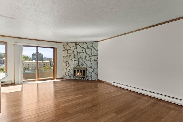 unfurnished living room with baseboard heating, a textured ceiling, hardwood / wood-style flooring, and a stone fireplace