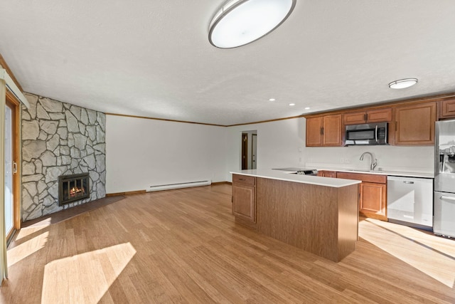 kitchen with sink, appliances with stainless steel finishes, a center island, baseboard heating, and a stone fireplace