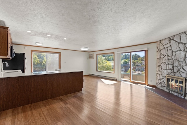 unfurnished living room featuring a textured ceiling, baseboard heating, light hardwood / wood-style flooring, and a stone fireplace