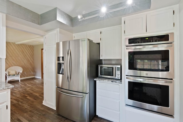 kitchen with appliances with stainless steel finishes, light stone countertops, wooden walls, dark hardwood / wood-style floors, and white cabinetry