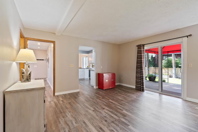 unfurnished room with a textured ceiling, beam ceiling, and hardwood / wood-style floors