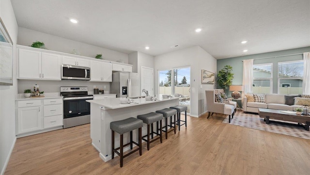 kitchen featuring stainless steel appliances, a center island with sink, a kitchen bar, light wood-type flooring, and white cabinets