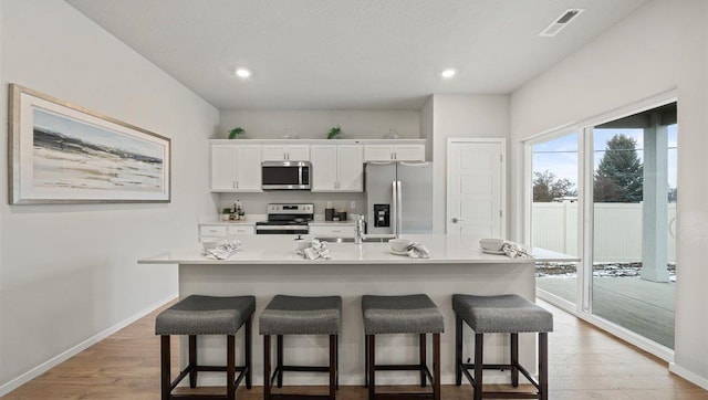 kitchen featuring stainless steel appliances, light hardwood / wood-style floors, a kitchen island with sink, white cabinets, and a kitchen breakfast bar