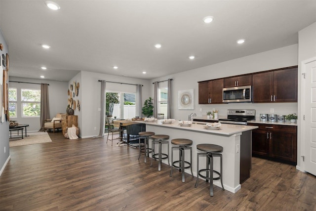 kitchen featuring sink, a breakfast bar area, a center island with sink, dark hardwood / wood-style flooring, and appliances with stainless steel finishes