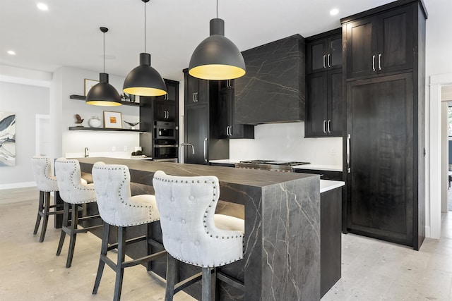 kitchen with a kitchen island with sink, wall chimney exhaust hood, a kitchen breakfast bar, and hanging light fixtures