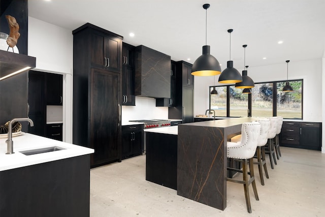 kitchen featuring wall chimney exhaust hood, decorative light fixtures, a center island with sink, a breakfast bar area, and sink