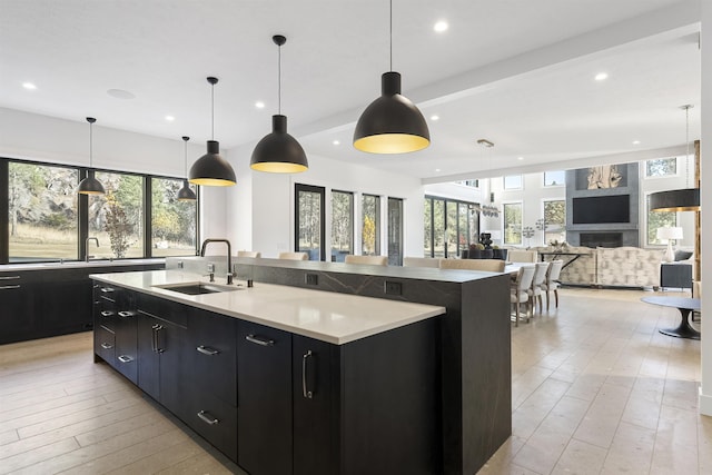 kitchen with a large island with sink, sink, hanging light fixtures, and light hardwood / wood-style flooring