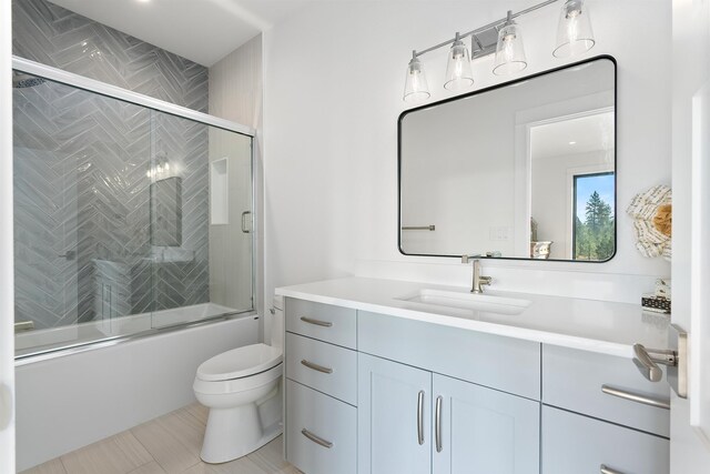 full bathroom featuring toilet, bath / shower combo with glass door, tile patterned floors, and vanity